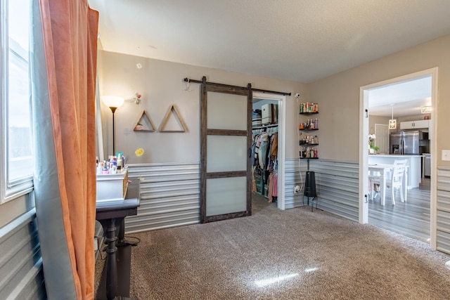 interior space featuring a barn door, carpet, a textured ceiling, stainless steel refrigerator with ice dispenser, and a closet