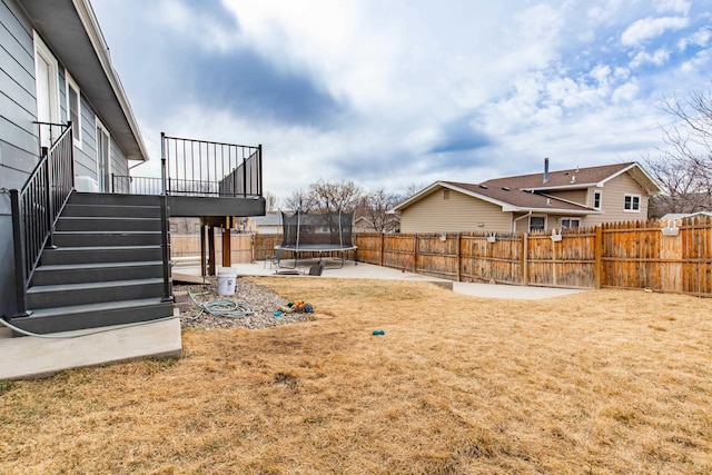 view of yard with a trampoline, a patio area, a deck, a fenced backyard, and stairs