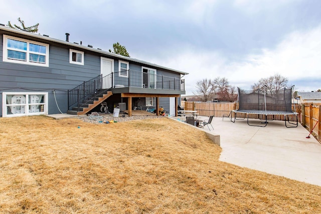 rear view of property featuring a trampoline, a yard, stairway, a patio area, and a fenced backyard