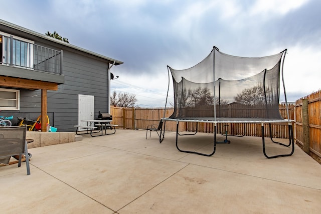 view of patio featuring a balcony, a fenced backyard, and a trampoline