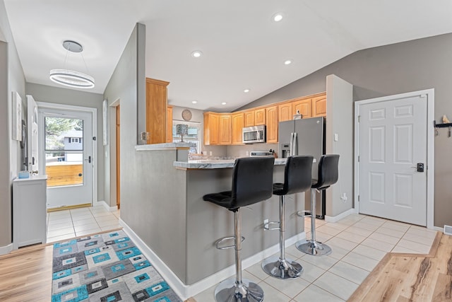 kitchen with light tile patterned floors, stainless steel appliances, vaulted ceiling, a peninsula, and a kitchen bar