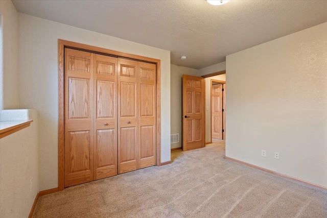 unfurnished bedroom featuring a textured ceiling, light carpet, visible vents, baseboards, and a closet