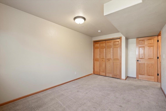 unfurnished bedroom featuring baseboards, a textured ceiling, a closet, and light colored carpet