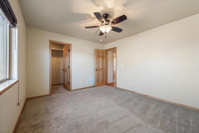 unfurnished bedroom with a walk in closet, light colored carpet, visible vents, ceiling fan, and baseboards