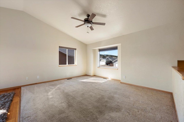 carpeted empty room featuring vaulted ceiling, ceiling fan, visible vents, and baseboards