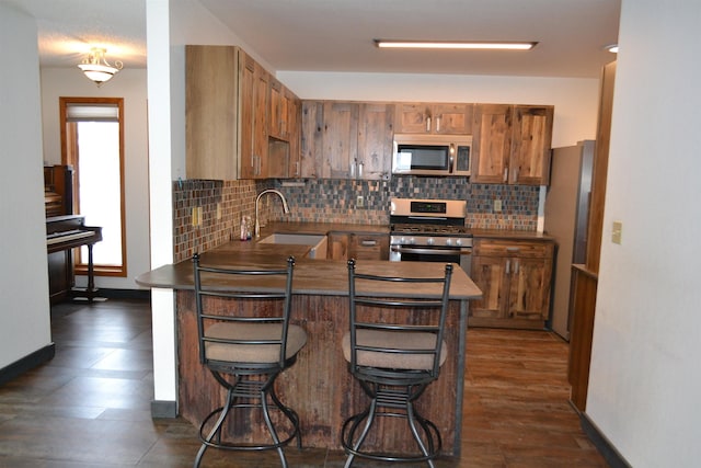 kitchen featuring brown cabinetry, decorative backsplash, appliances with stainless steel finishes, a peninsula, and a sink