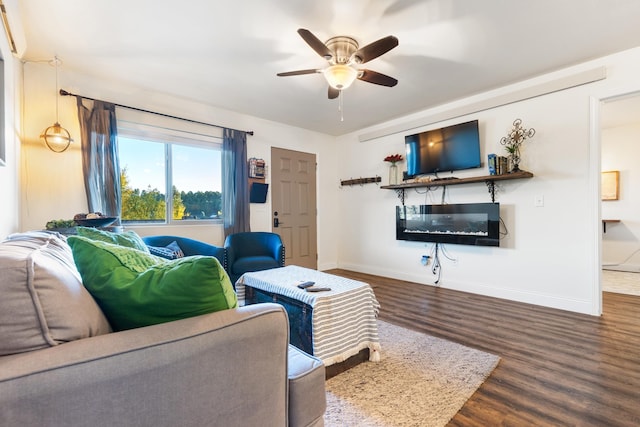 living area featuring ceiling fan, a glass covered fireplace, wood finished floors, and baseboards