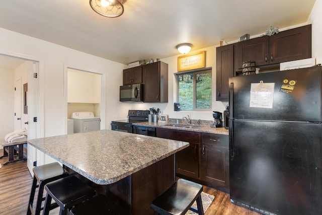 kitchen with washer and clothes dryer, dark brown cabinetry, a sink, black appliances, and a kitchen bar