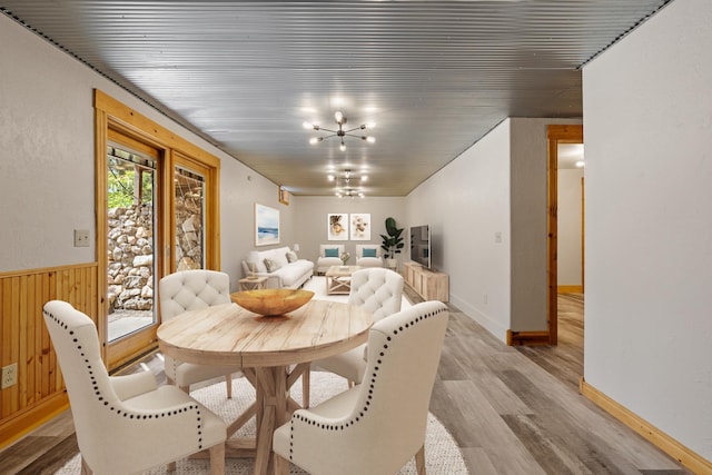 dining area with a notable chandelier, wainscoting, light wood-style flooring, and wooden walls