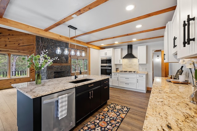 kitchen featuring decorative backsplash, appliances with stainless steel finishes, wood finished floors, wall chimney range hood, and a sink