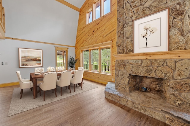 dining area with a fireplace, a towering ceiling, wooden walls, wood finished floors, and baseboards