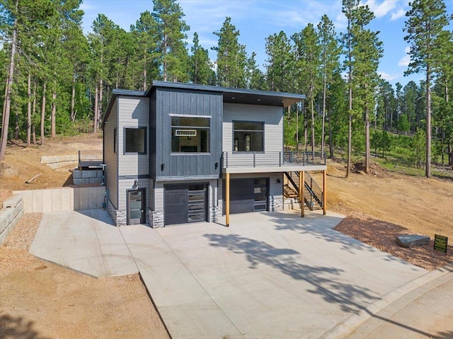 contemporary home featuring board and batten siding, a garage, stone siding, driveway, and stairs