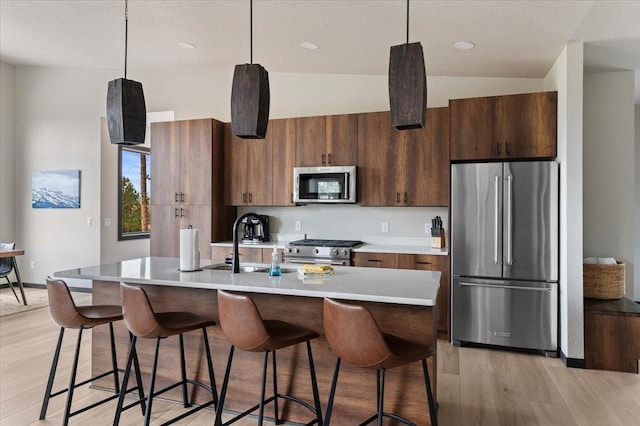 kitchen with a breakfast bar area, light wood-style flooring, stainless steel appliances, light countertops, and an island with sink