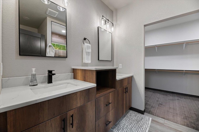 bathroom featuring a walk in closet, visible vents, a sink, and double vanity