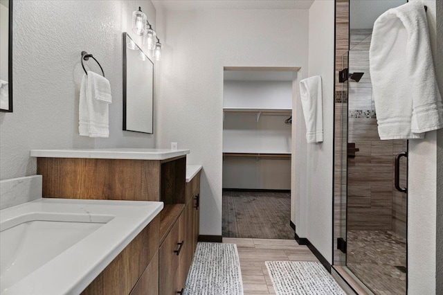 bathroom featuring a stall shower, wood tiled floor, a walk in closet, and vanity