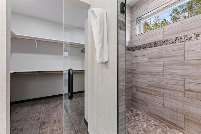 full bath with tiled shower, wood finished floors, a walk in closet, and baseboards