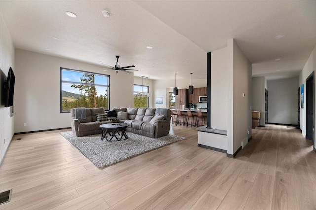 living room featuring a ceiling fan, baseboards, light wood-style flooring, and a textured ceiling