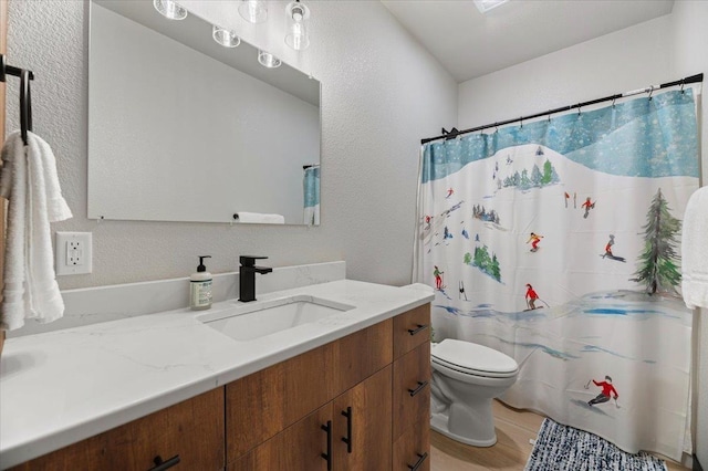 bathroom with a textured wall, wood finished floors, vanity, and toilet