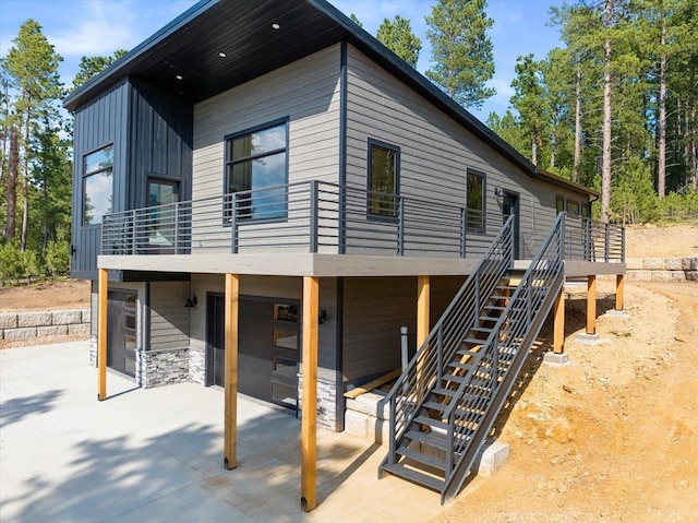 back of property with a patio, an attached garage, driveway, stairway, and board and batten siding