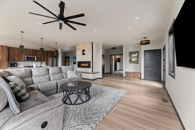 living area featuring lofted ceiling, ceiling fan, a fireplace, visible vents, and light wood-style floors