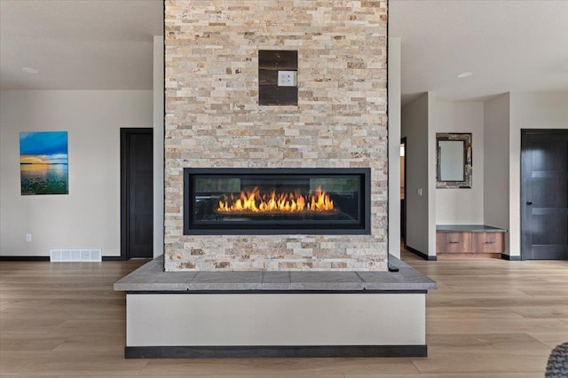 room details with baseboards, visible vents, wood finished floors, and a stone fireplace