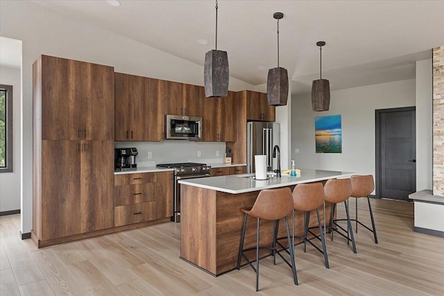 kitchen with light countertops, premium appliances, a sink, and light wood-style floors