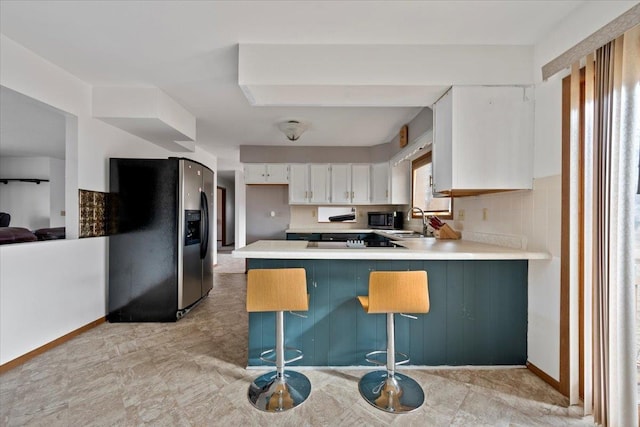 kitchen featuring a peninsula, a sink, refrigerator with ice dispenser, white cabinets, and light countertops