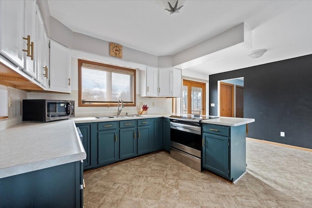 kitchen featuring white cabinets, a peninsula, blue cabinets, stainless steel appliances, and a sink