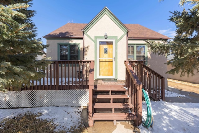 view of front of house with roof with shingles, a wooden deck, and stucco siding