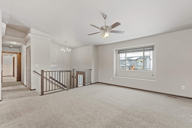 carpeted spare room featuring ceiling fan with notable chandelier and baseboards