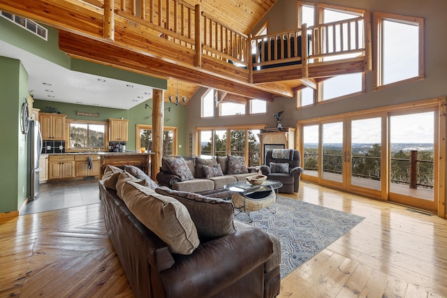 living room featuring visible vents, a tiled fireplace, light wood-style flooring, french doors, and high vaulted ceiling