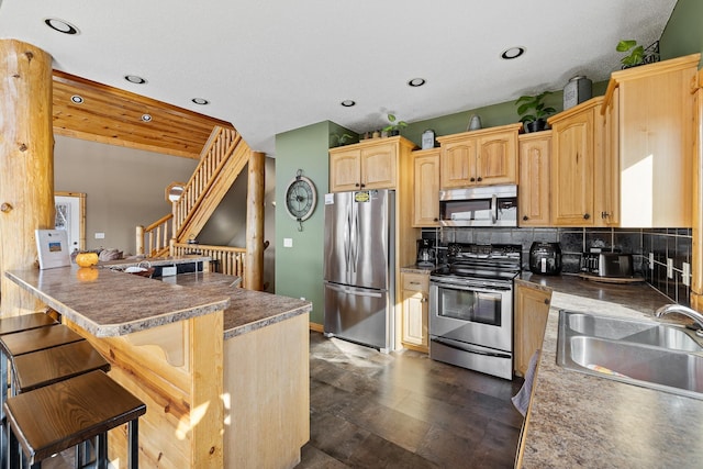 kitchen featuring stainless steel appliances, a sink, a kitchen breakfast bar, light brown cabinetry, and tasteful backsplash