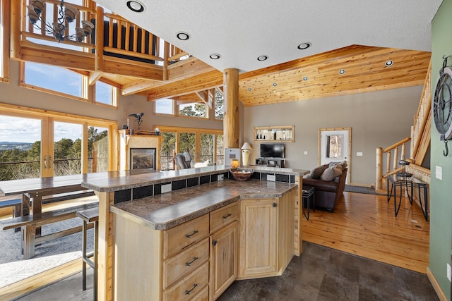 kitchen with a tile fireplace, dark countertops, open floor plan, light brown cabinetry, and high vaulted ceiling