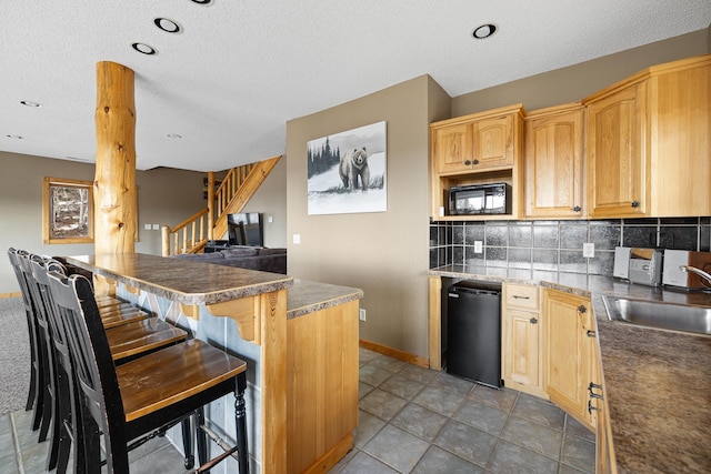 kitchen featuring black microwave, light brown cabinets, a sink, tasteful backsplash, and a kitchen bar