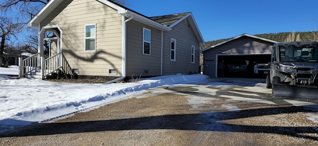 view of snow covered exterior featuring a garage, crawl space, and an outbuilding