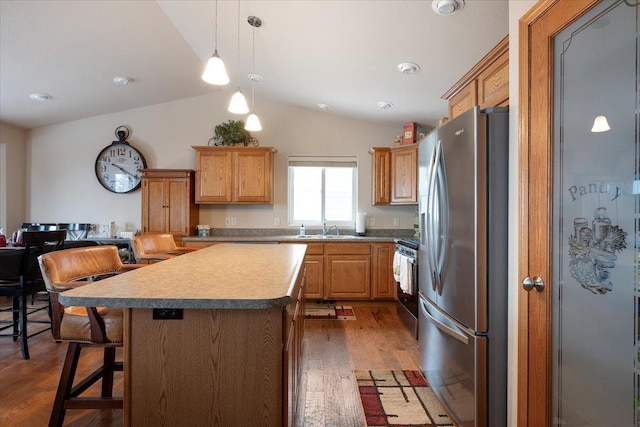 kitchen featuring a center island, appliances with stainless steel finishes, wood finished floors, a sink, and lofted ceiling
