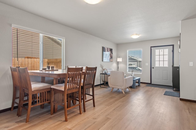 dining space with a textured ceiling, light wood-style flooring, and baseboards