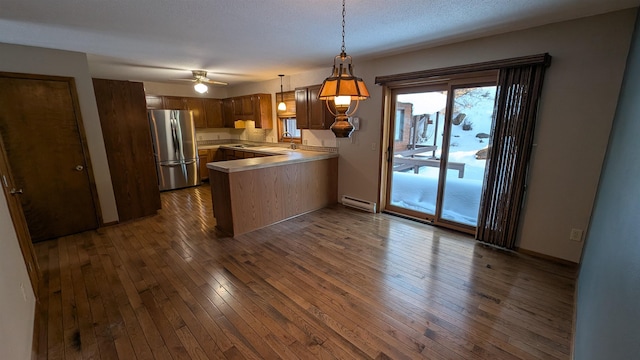 kitchen featuring a baseboard radiator, dark wood-style flooring, freestanding refrigerator, a peninsula, and light countertops