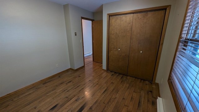 unfurnished bedroom with a baseboard heating unit, hardwood / wood-style floors, and a closet