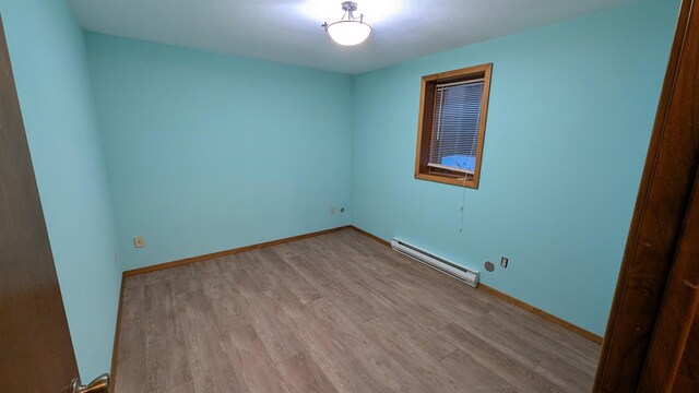 unfurnished room with a baseboard radiator, baseboards, and wood finished floors