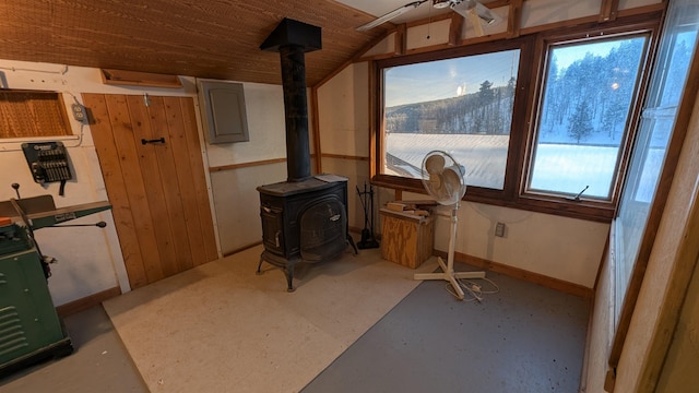 interior space featuring lofted ceiling, a ceiling fan, baseboards, electric panel, and a wood stove