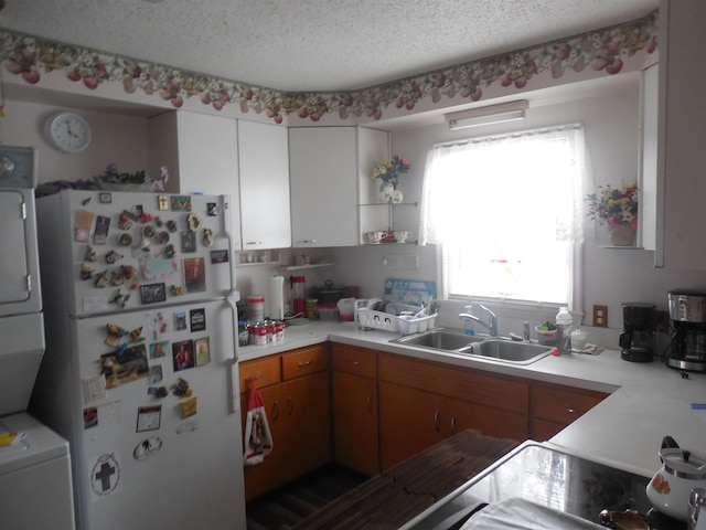 kitchen featuring stacked washer and clothes dryer, freestanding refrigerator, light countertops, a textured ceiling, and a sink