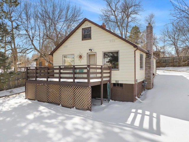 snow covered back of property with a chimney, fence, and a deck