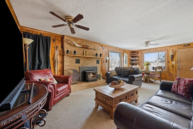living area with carpet floors, a wood stove, ceiling fan, wooden walls, and a textured ceiling