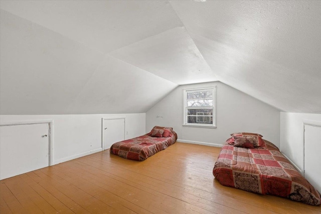bedroom with vaulted ceiling, a textured ceiling, wood-type flooring, and baseboards