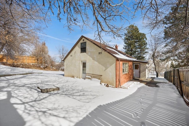 snow covered property featuring brick siding, fence, a chimney, and stucco siding