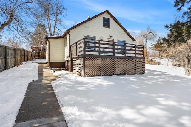 snow covered back of property with fence and a wooden deck