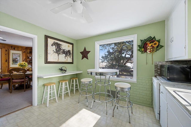 dining room with a ceiling fan, wainscoting, wood walls, and light floors