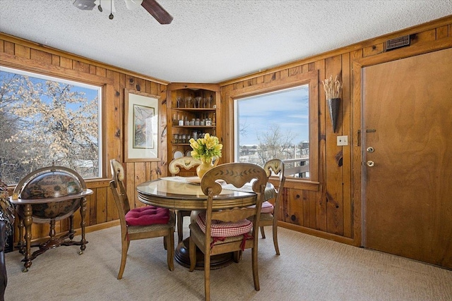 dining area featuring a textured ceiling, built in shelves, wood walls, and light carpet