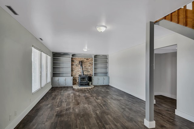 unfurnished living room with visible vents, baseboards, a wood stove, and dark wood-type flooring